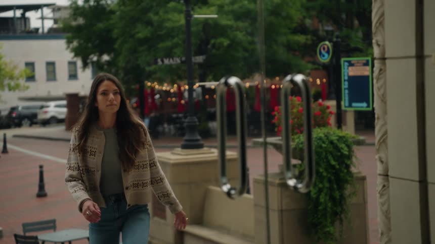 A woman walks through an urban plaza and enters a building with calm deliberate motion