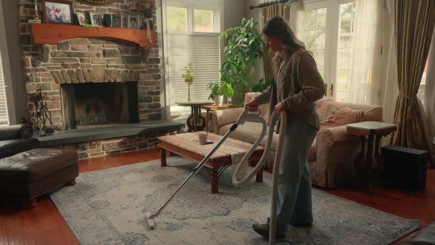 Woman cleans a rug in a living room with a vacuum cleaner