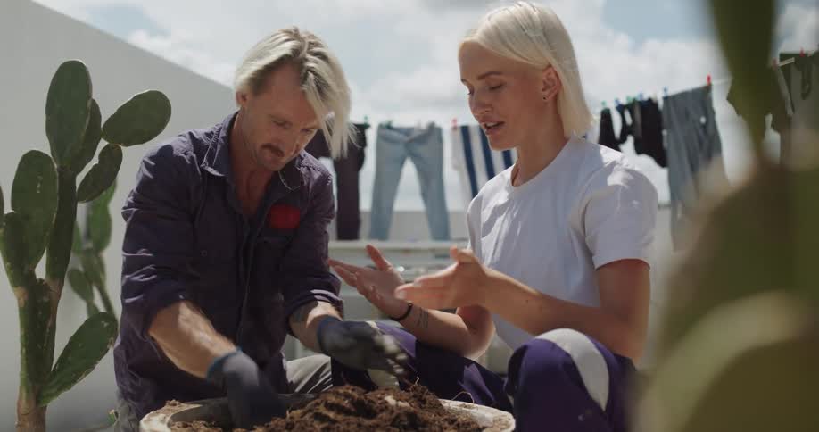 Man wearing gloves and woman digging a hole in a potted plant