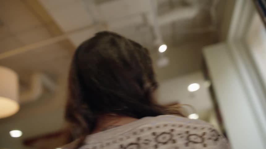 A woman walking through a library with a book in her hand looking at the shelves