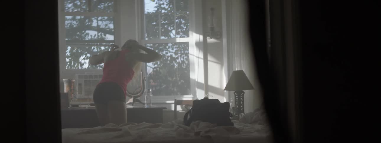 A woman puts on a red shirt and picks up a water bottle
