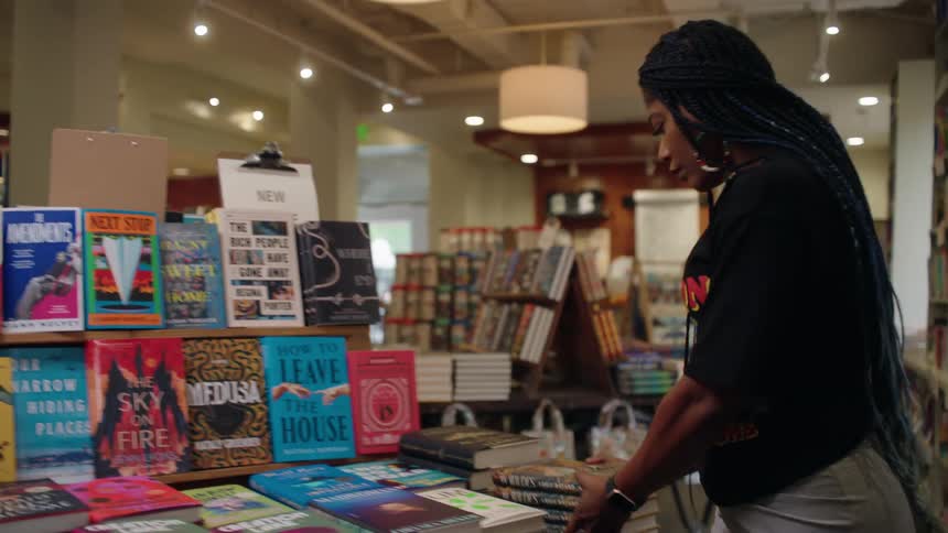 A black woman carries books to a table while working in a book store