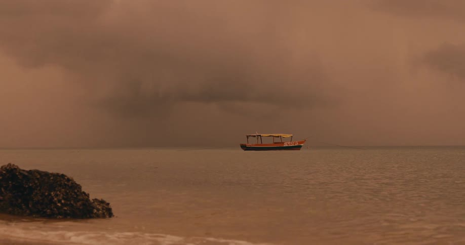 Empty boat floating off the coast under a cloudy sunset sky