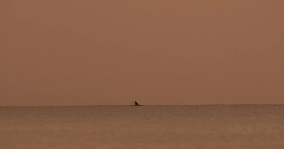 A lone boat drifts on a calm ocean beneath an orange sky evoking solitude