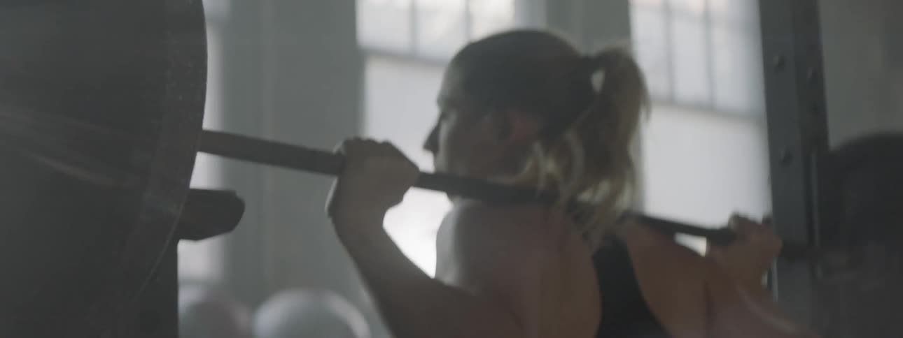 A woman lifting a barbell weight in a building and placing it back on the bar