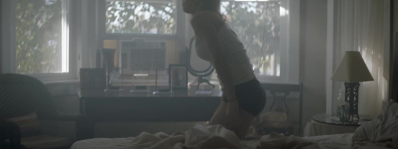 A woman sits on a bed and then stands up