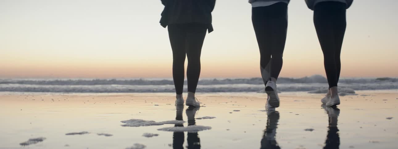 A group of women walk across the sand toward the waves and stand to watch at dusk