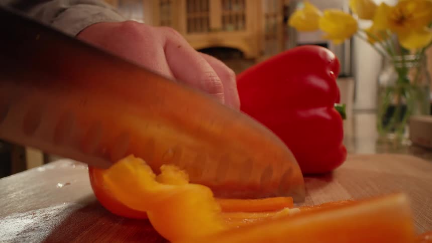 Hands of a lady cutting fruits with a knife in the kitchen at night