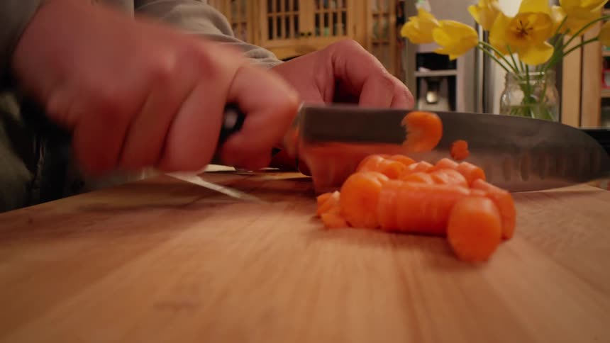 Pair of hands with a knife cutting carrot slices on top of a cutting board