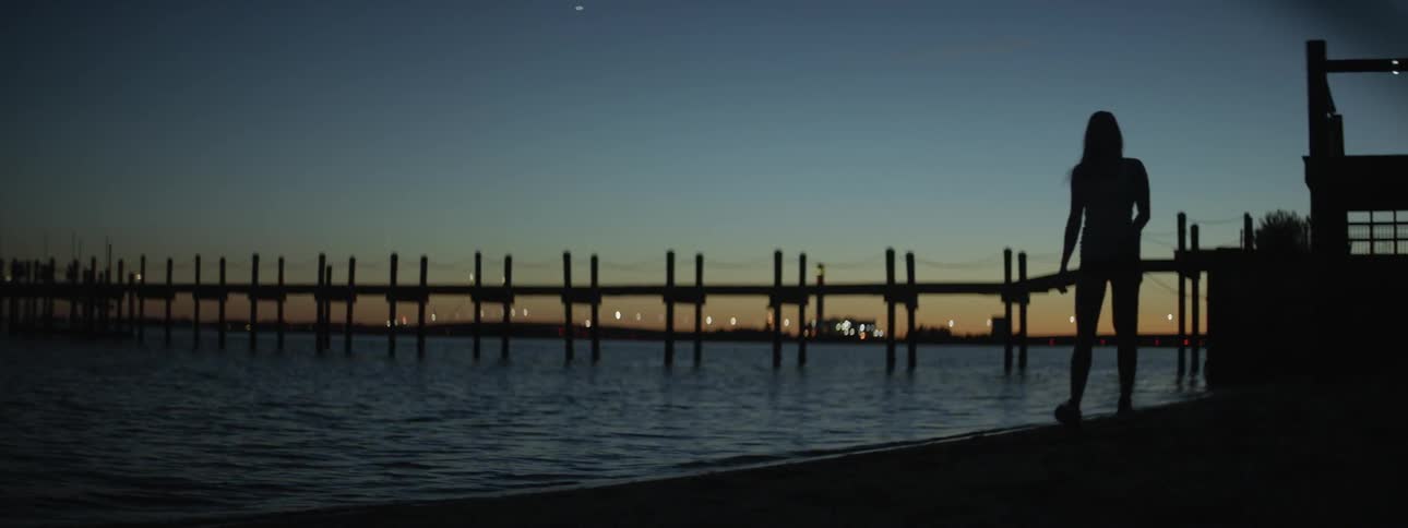 A view of a bridge over water and lights in the background at dusk
