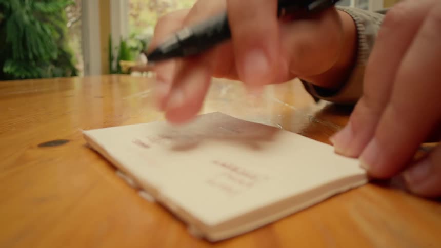 A person at a table writing with a pen in a notepad