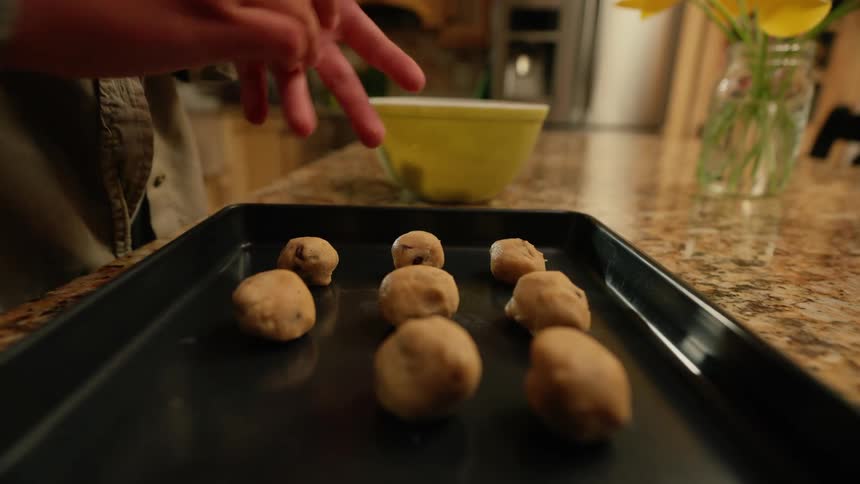 An adult makes dough balls while baking cookies in a kitchen