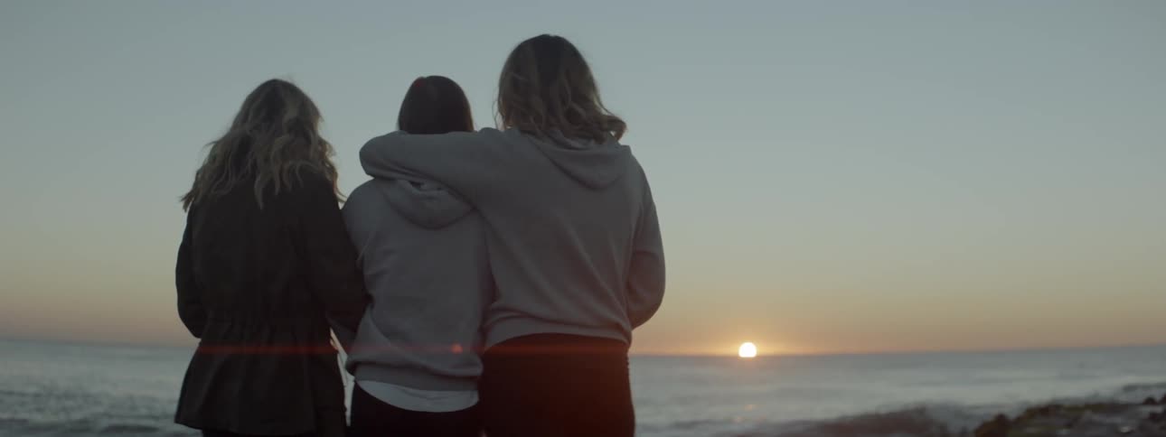 A group of three people standing and looking out over the water at the sun