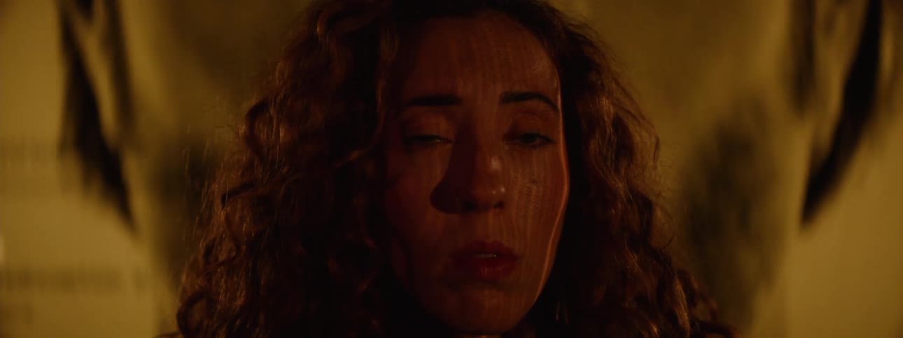 The face of a woman who has a worried facial expression and with her eyes closed then she opens them and several yellow lights are hitting her face