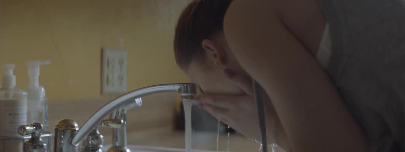Woman turns on sink faucet in kitchen to splash water on her face