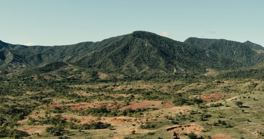 A wide scenic view of green mountains and red earth plains under a clear sky