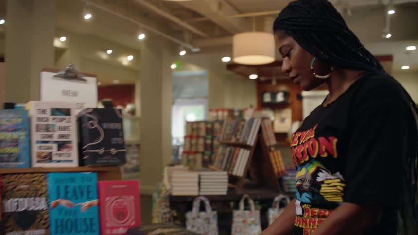 Woman carrying a stack of books through a bookstore