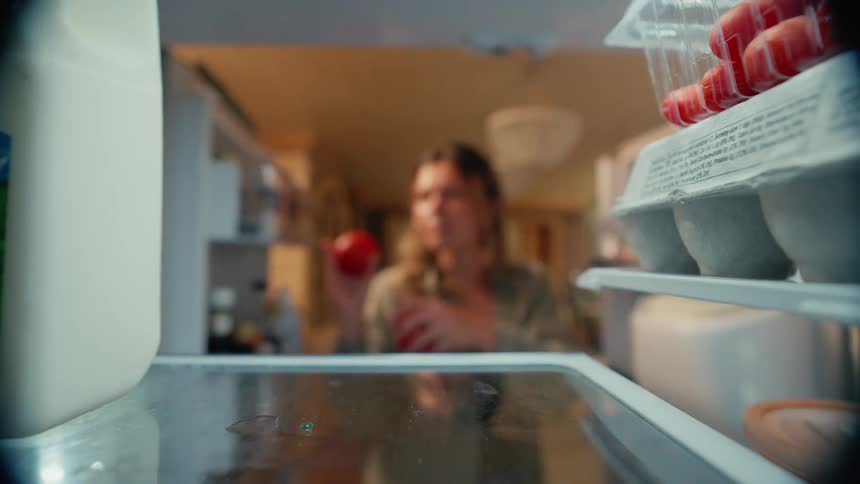 Point of view woman reaching into refrigerator grabbing two tomatos from glass shelf