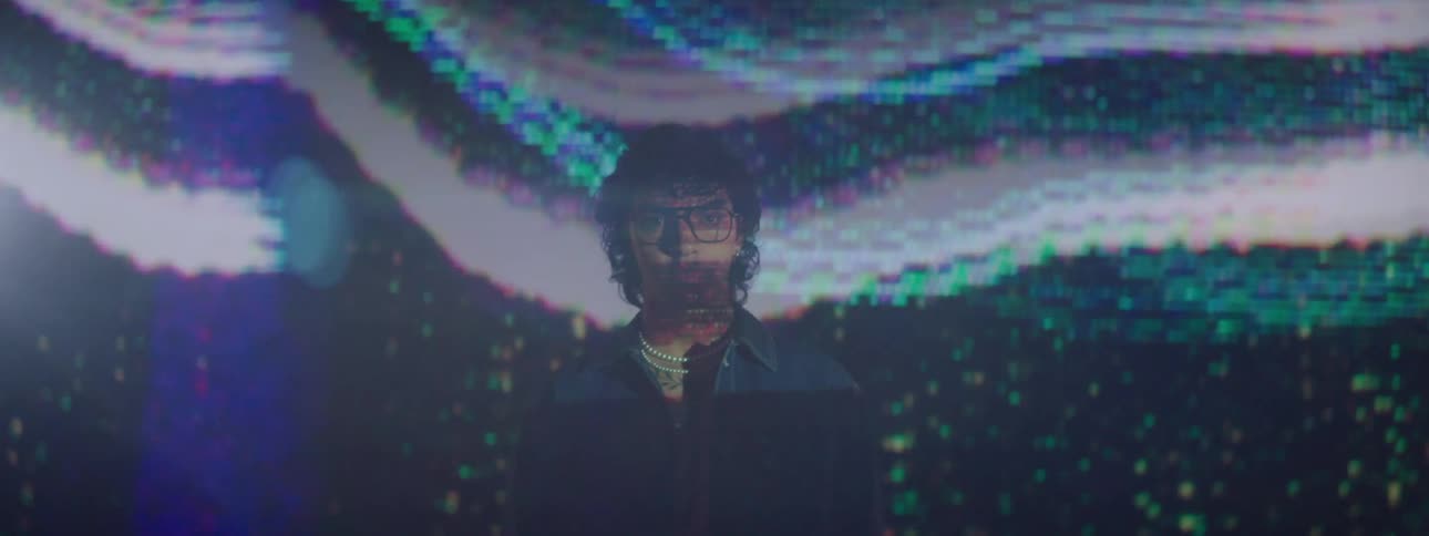 A young man wearing eyeglasses is standing in front of a projector screen