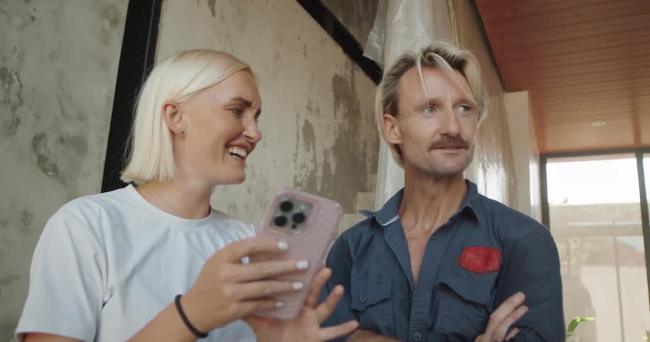 A woman smiles while showing something on her phone to a man during a casual work conversation