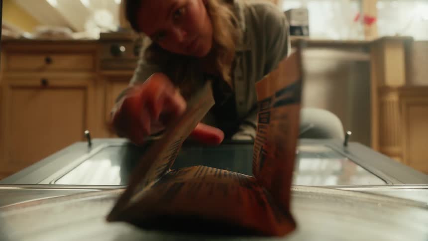 POV from inside a microwave as a woman opens the door, places an unpopped bag of popcorn in and then closes the door.