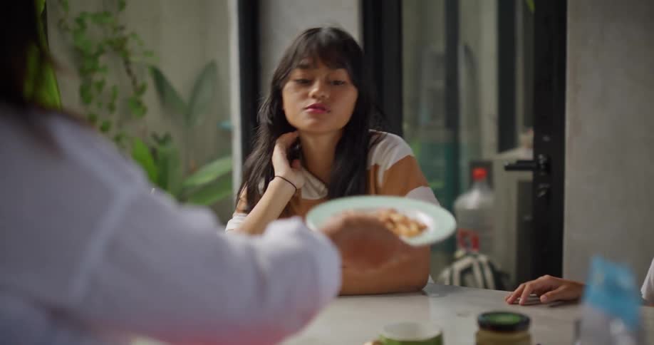 Two girls gets seated at the dinner table with food being served by the mother