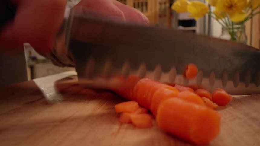 A person in a kitchen cutting carrots on a table