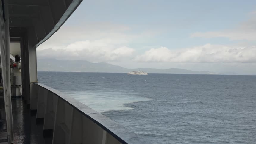 A view from the deck of a ship looking out over the open ocean with distant mountains under a partly cloudy sky