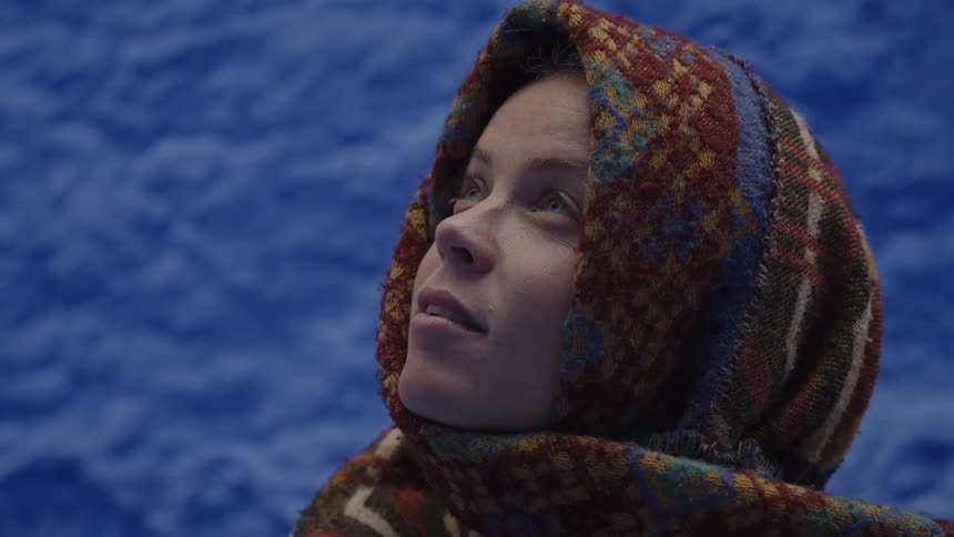 A woman putting a reddish decorated scarf on her head and looking up