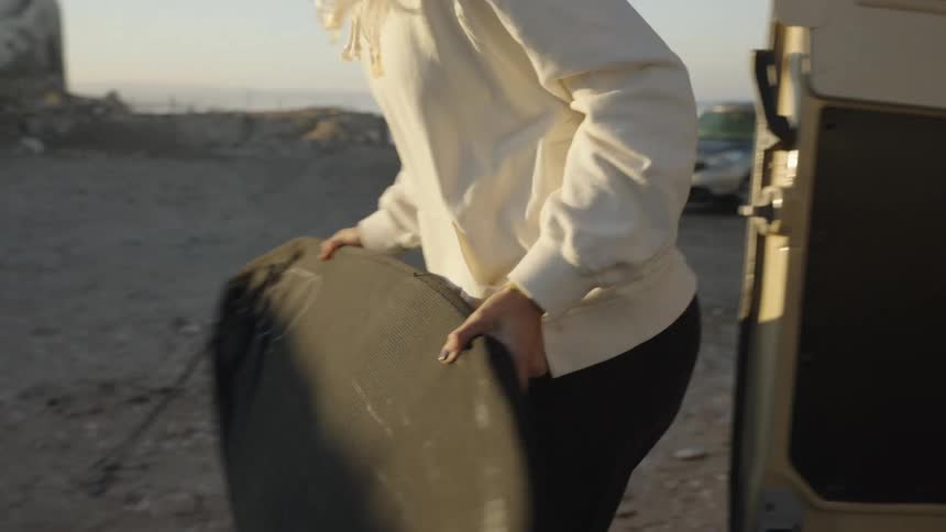 A young woman stacks surfboards on the floor at midday