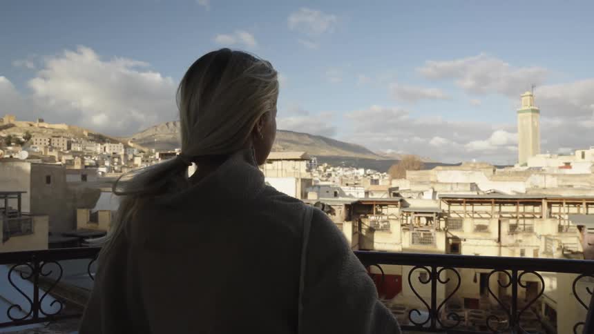 Woman on a balcony enjoying the view of a city with mountains in the background