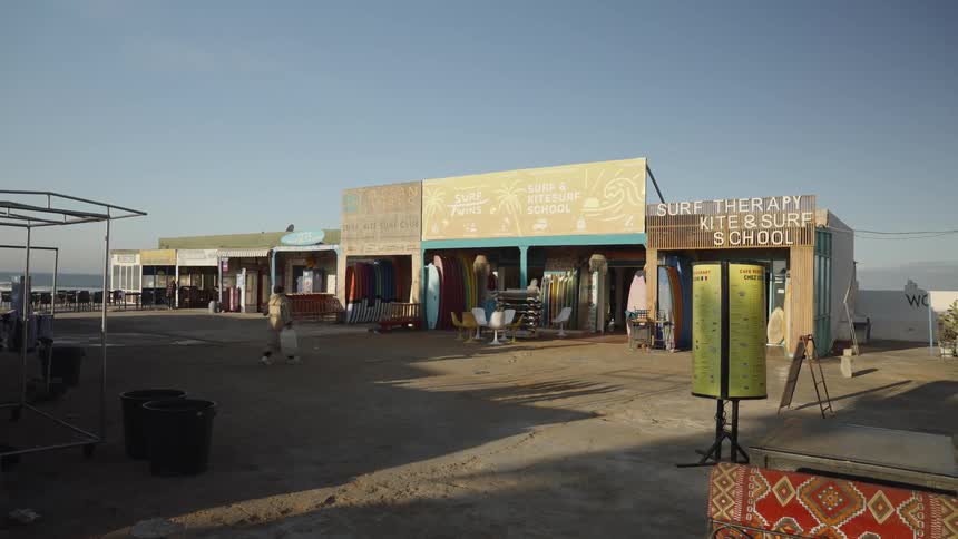 A woman holding a shopping bag walks from one store to another in a small plaza with tiny shops