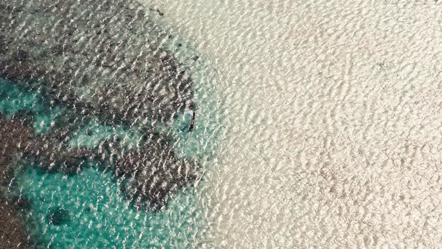 An aerial view shows a contrast between dark rocky formations in turquoise water