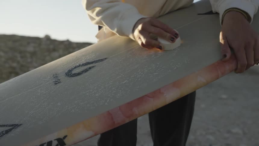 Blonde female surfer waxing surface of her surfboard at the beach