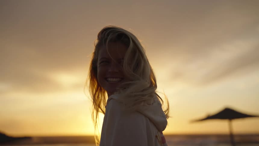 A woman laughs on the beach at sunset