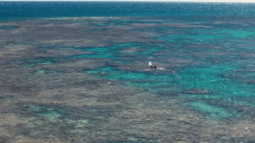A small boat sails over a vibrant coral reef in clear tropical water seen from above