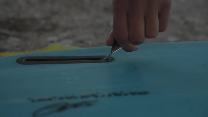 A person turns a key into a groove on a surfboard