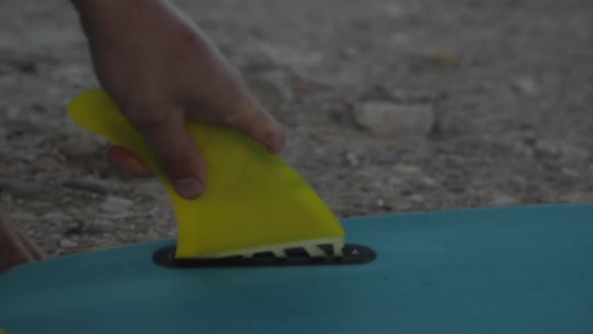 A man attaches fins to his surfboard