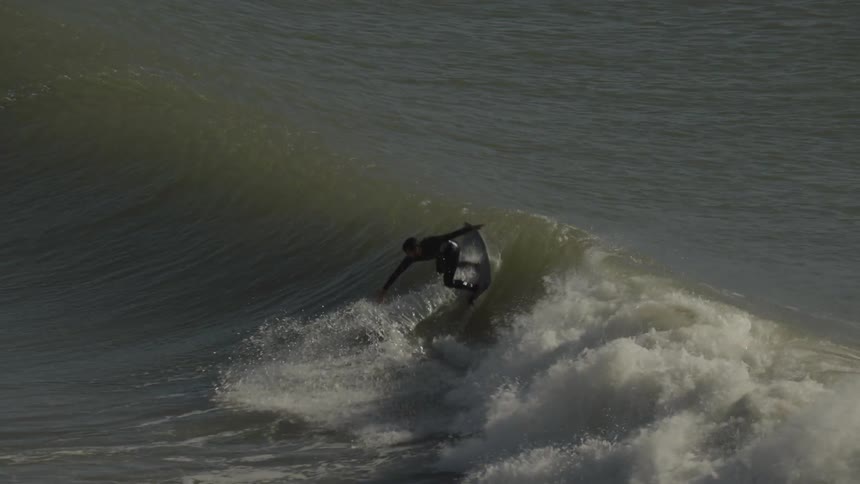 A man surfing a wave and performing a trick while another man lies on his board nearby