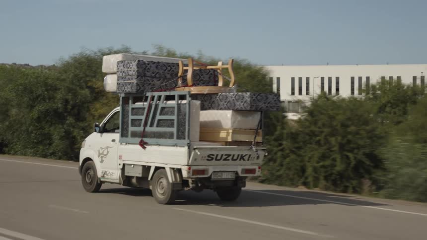 A white truck loaded with furniture is driven on the road in daytime