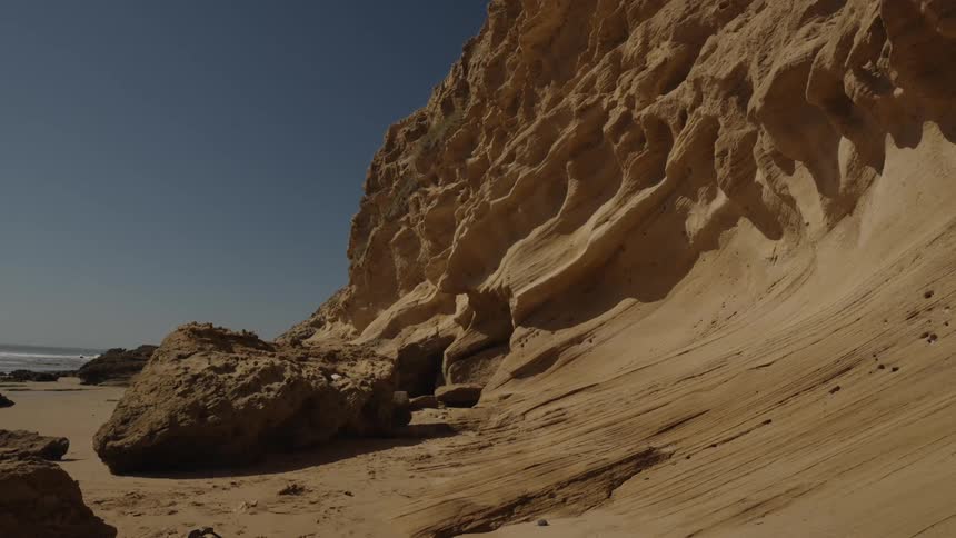 A wide shot of rugged coastal cliffs and a sandy beach under a clear blue sky