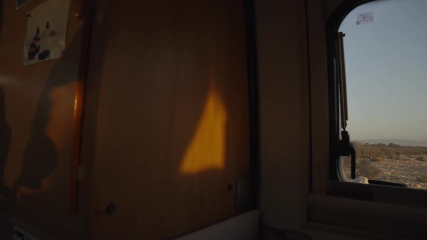 The interior of a vehicle with wooden walls and a huge window that gives a view of a desert environment