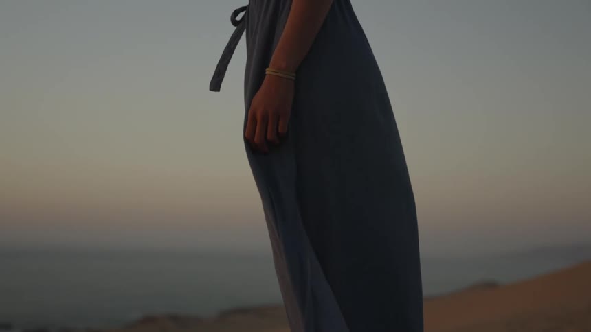 A woman standing still on the sand gazing at the sea