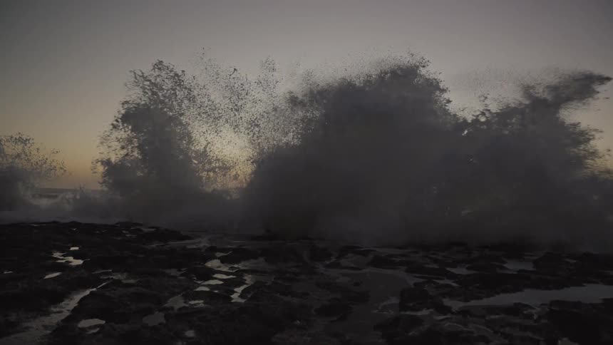Waves roll in to shore and splash high in the air as they crash against the coast