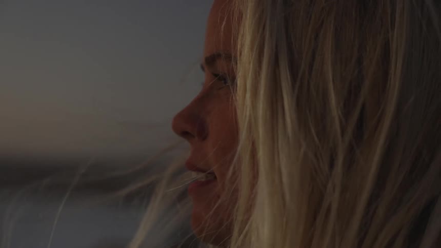 A woman with a slight smile lost in thought her hair blowing in the wind