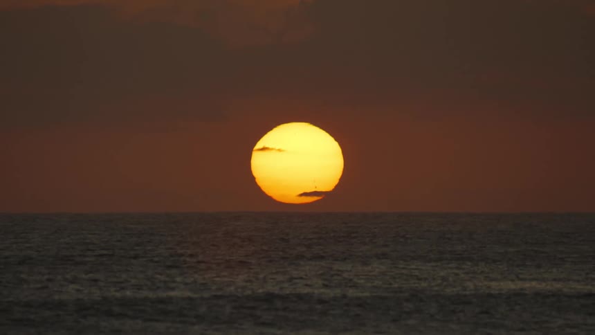 Sun glowing over the water on the horizon in a deep red sky