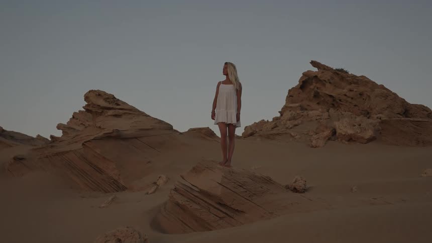 Woman standing on a rock on a hill near rock formations in the desert