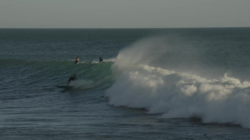 A surfer rides a powerful wave as others wait in the ocean nearby under clear skies