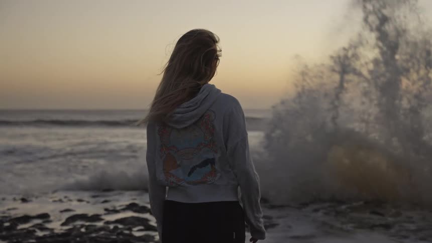 Young woman walking along the coast as waves splash against rocks