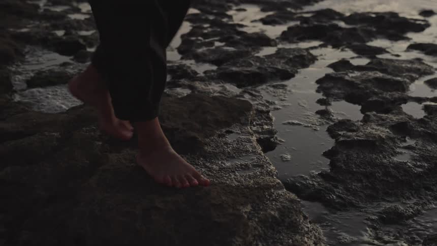 Bare feet step across wet coastal rocks at dusk evoking quiet connection with nature
